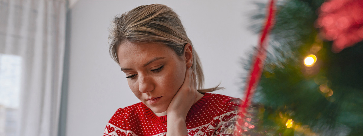 a woman sitting on a couch next to a christmas tree looking sad.