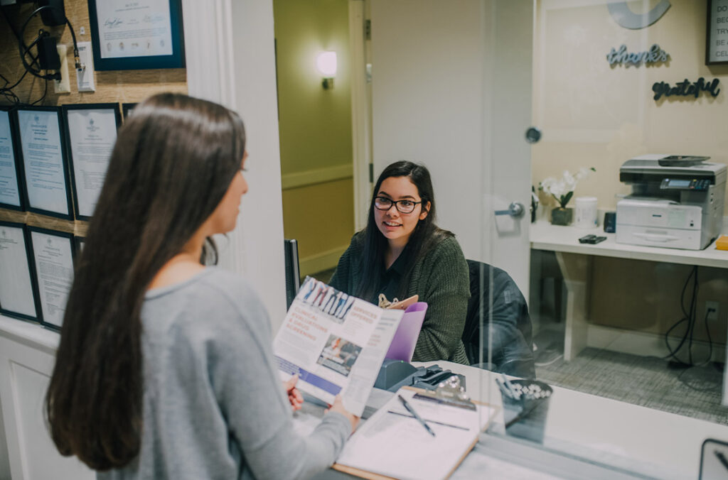 a woman reading a brochure and another woman behind a dest sitting down